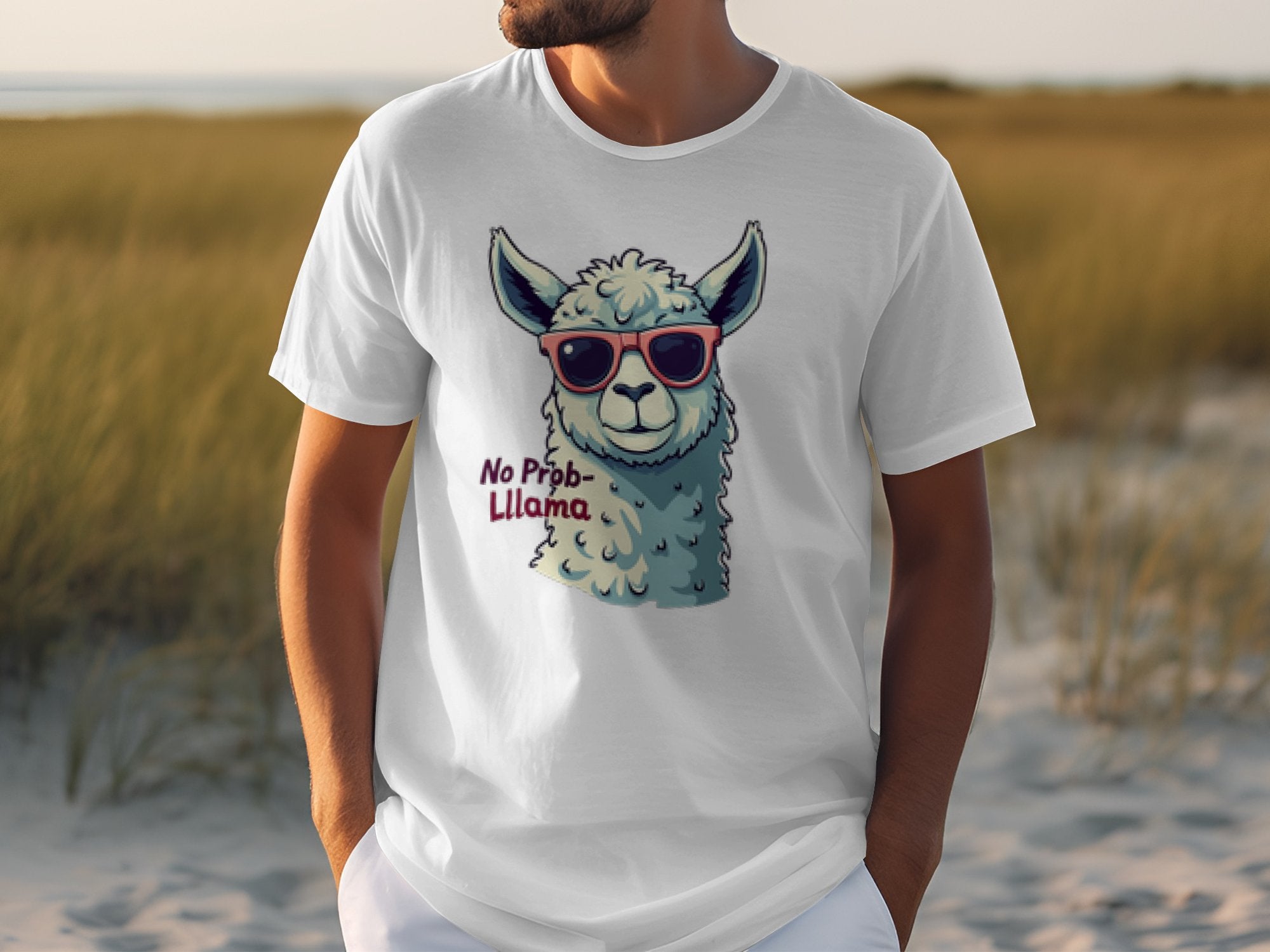 In a grassy field, someone wears a white Garment Graphics Llama T-Shirt featuring a cartoon llama in sunglasses with the text No Prob-Llama. This playful design adds whimsy to any casual outing and is great for matching family outfits.