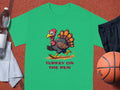 This Garment Graphics classic fit green t-shirt features a humorous turkey running and the phrase TURKEY ON THE RUN below. Perfect for sports enthusiasts, it’s displayed with a water bottle, white towel, black shorts, and a basketball on the sports surface.