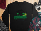 Garment Graphics festive sweatshirt showcases a green truck packed with shamrocks and Happy St. Patricks Day text, surrounded by a red beanie, gloves, black-and-white scarf, and green plaid shirt on wood.