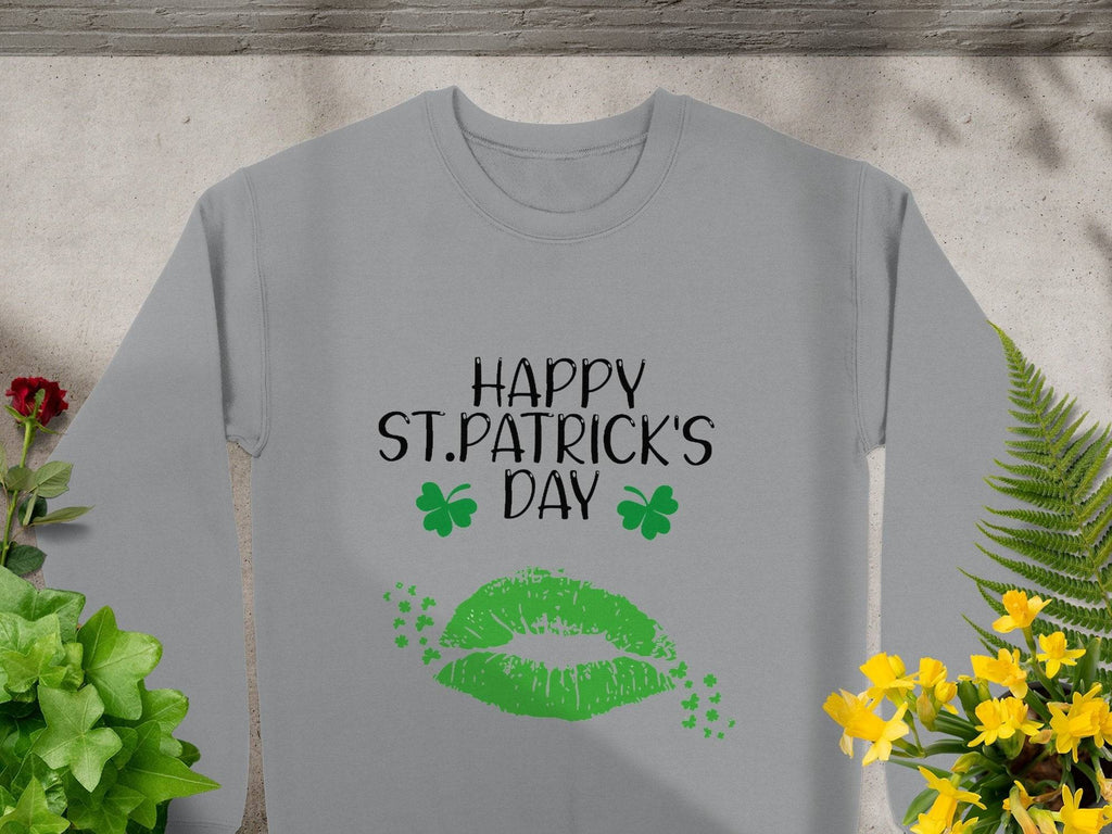 Garment Graphics offers a gray sweatshirt featuring Happy St. Patricks Day in black, above green lips with two clover kisses, artfully displayed among plants and flowers on a stone surface, capturing the festive spirit.