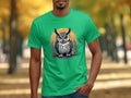 In a picturesque autumn setting, a person stands outside wearing Garment Graphics green T-shirt, featuring an owl with large eyes on an orange circular background. The scene exudes artistic flair amid the vibrant fall foliage.