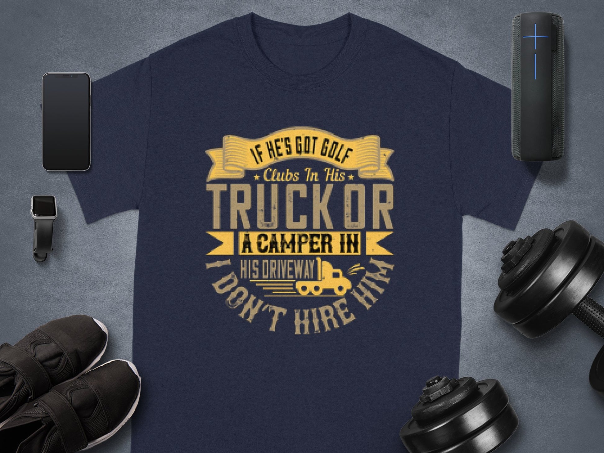 Garment Graphics presents a navy blue T-shirt featuring the quote If hes got golf clubs in his truck or a camper in his driveway, I dont hire him in yellow and white. Accompanied by essentials like a smartwatch, shoes, weights, a portable speaker, and earphones—ideal for golf lovers.