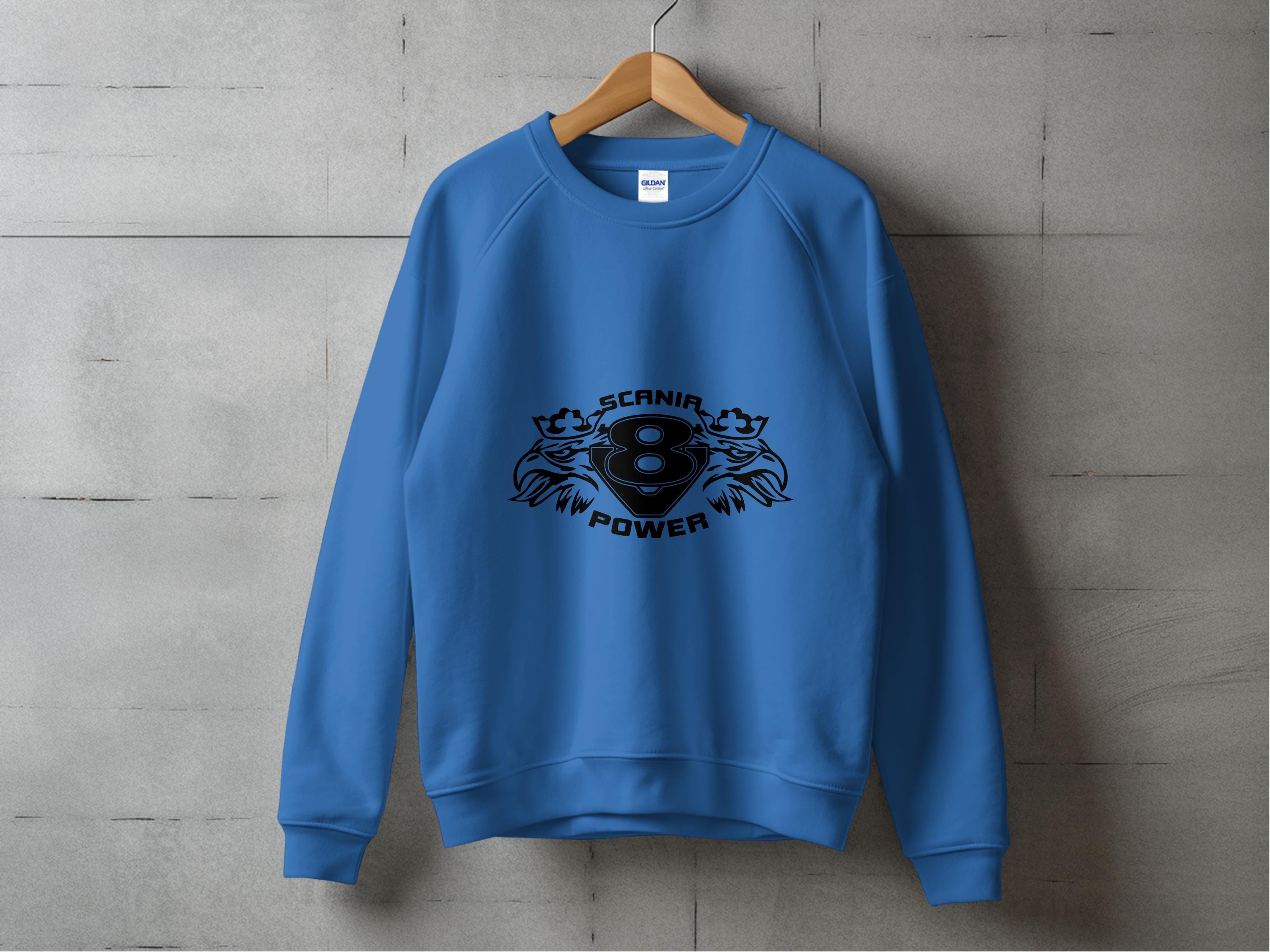 A blue sweatshirt from Garment Graphics hangs on a wooden hanger against a concrete wall, featuring a cool black design with the stylized number 8, SCANIA, and POWER beneath two lions, capturing the essence of Scania Power V8 sweatshirts.