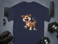 A navy blue T-shirt by Garment Graphics, featuring a playful brown and white cartoon dog surrounded by a smartphone, smartwatch, black shoes, portable speaker, and dumbbells on a gray surface; perfect for dog lovers.