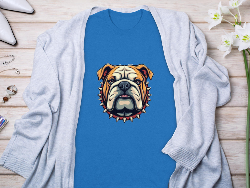 A cool blue Garment Graphics t-shirt featuring a bulldog design with a spiked collar detail is stylishly laid out on a wooden surface. Its complemented by a light gray cardigan, chic white heels, a bracelet, and delicate white flowers—ideal for enhancing any outfit with its bold flair.