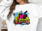 Wearing a Garment Graphics sweatshirt with a graffiti design, the text I ♥ Graffiti appears amid vibrant splashes of blue, pink, and yellow. The persons face is obscured by their wavy hair flowing over the urban style piece.