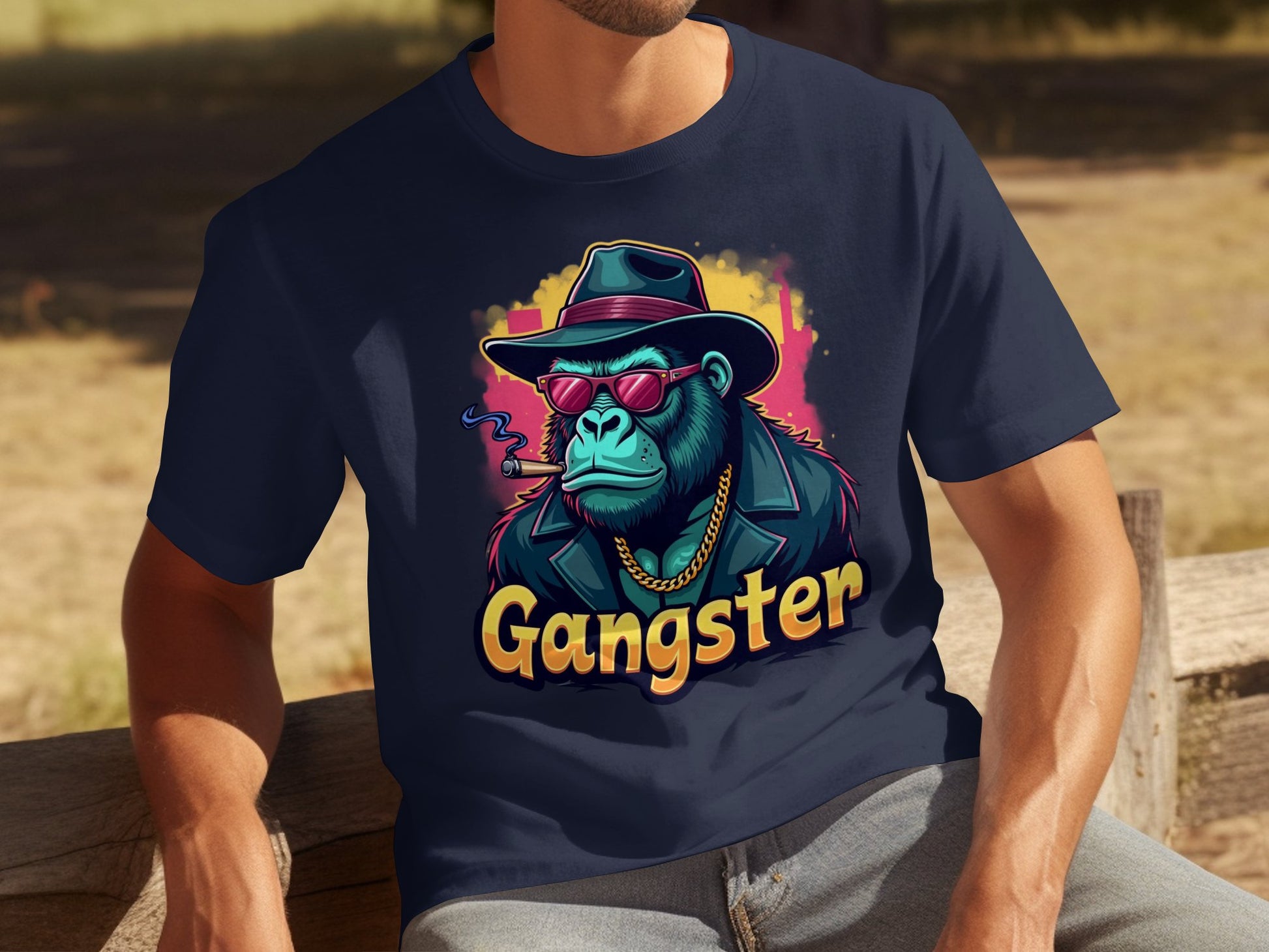 A person is on a wooden bench in a navy Gangster Gorilla T-shirt by Garment Graphics. The classic fit features a gorilla illustration with sunglasses, urban gangster style, hat, gold chain, smoking cigar, and Gangster boldly displayed below.
