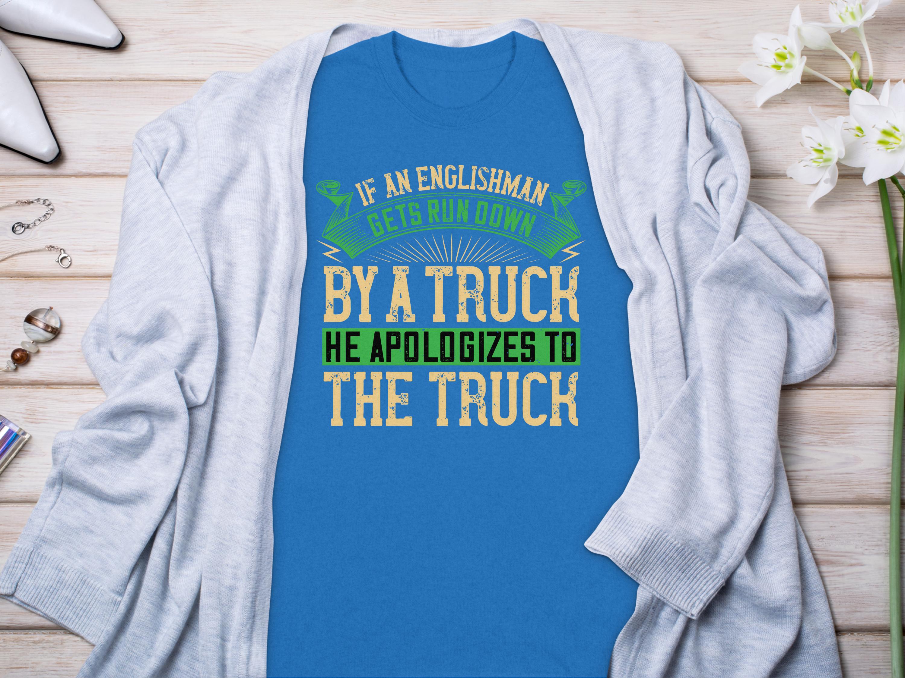A Garment Graphics blue T-shirt with the humorous design If an Englishman gets run down by a truck, he apologizes to the truck is paired with a gray cardigan. Nearby sit white flowers, perfume, and silver high heels, highlighting Englishmans politeness humorously.