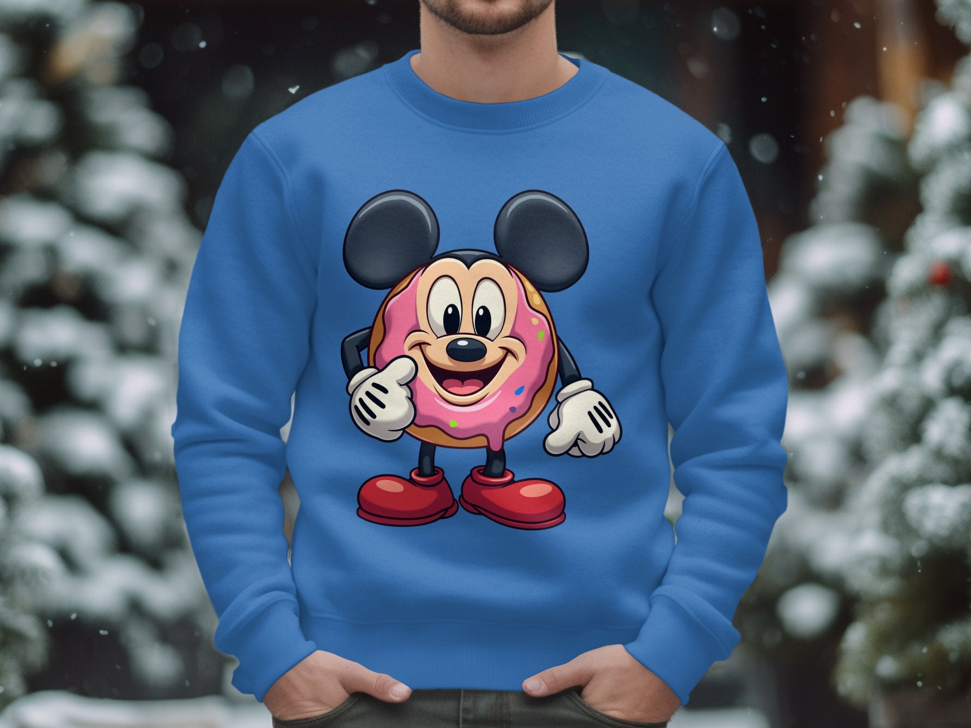 Standing outside in the snow, a person is wrapped in a playful Garment Graphics sweatshirt featuring a cute cartoon donut character. With mouse ears, pie eyes, sprinkle-covered face, white gloves, and red shoes, they add charm as blurred trees form the background.