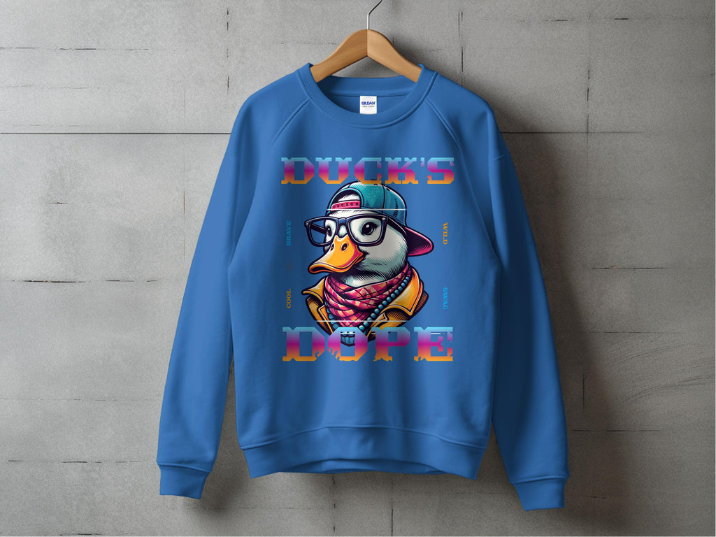 Against a gray wall, a blue sweatshirt from Garment Graphics hangs on a wooden hanger. It features a stylish cartoon duck in sunglasses, cap, and scarf with DUCKS DOPE printed in colorful bold letters, offering a bold fashion statement for any wardrobe.