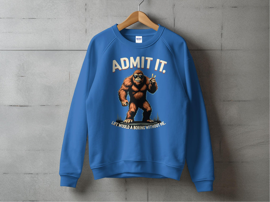 The image shows a Garment Graphics blue sweatshirt on a hanger against a gray wall, featuring a Bigfoot graphic with ADMIT IT and Life would be boring without me. This unisex casual wear item humorously enhances any wardrobe.