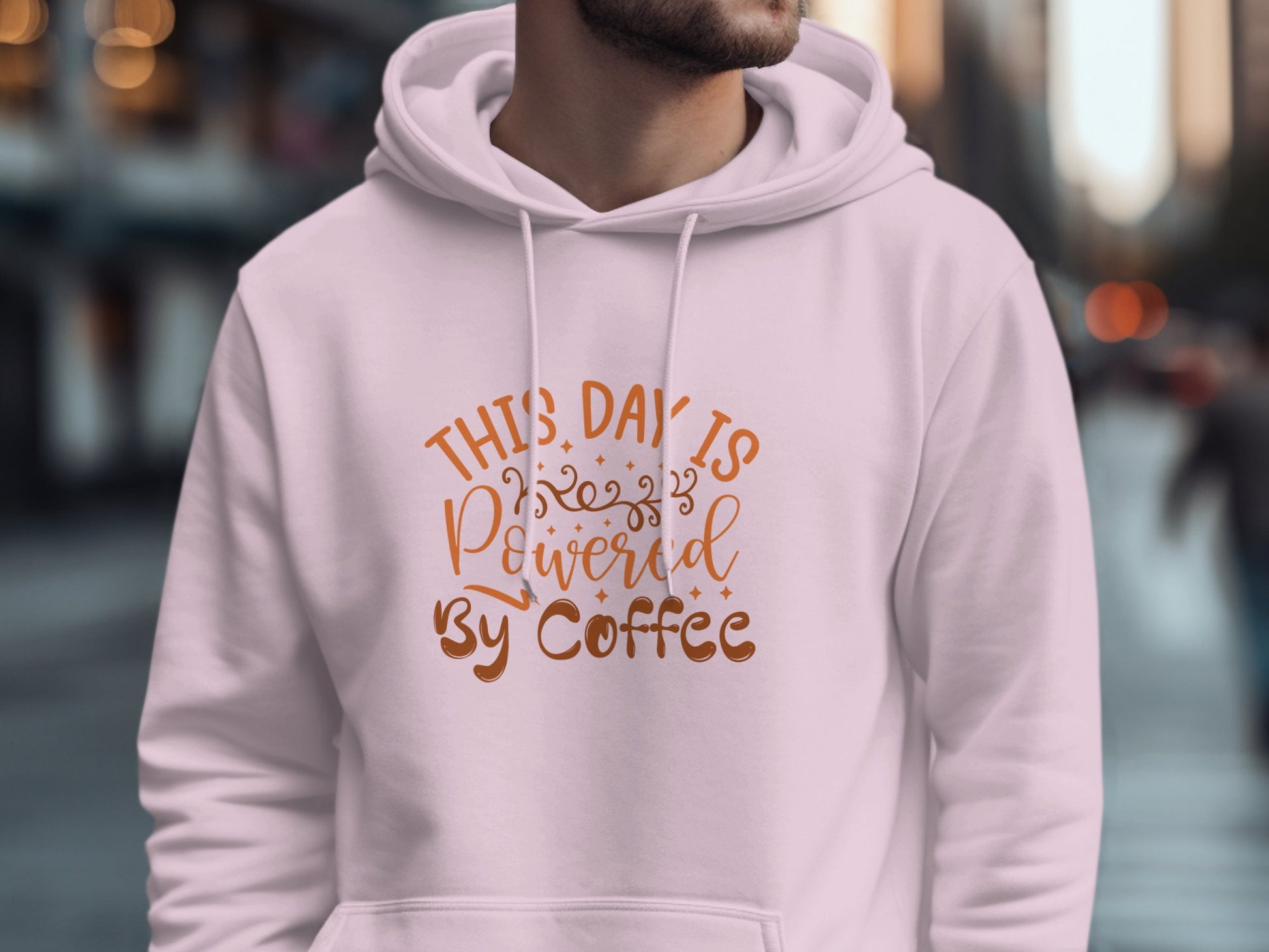 Sporting a chic white Garment Graphics hoodie emblazoned with This day is powered by coffee in vibrant orange, a coffee lover stands against a dreamy, blurred cityscape of buildings and passersby.