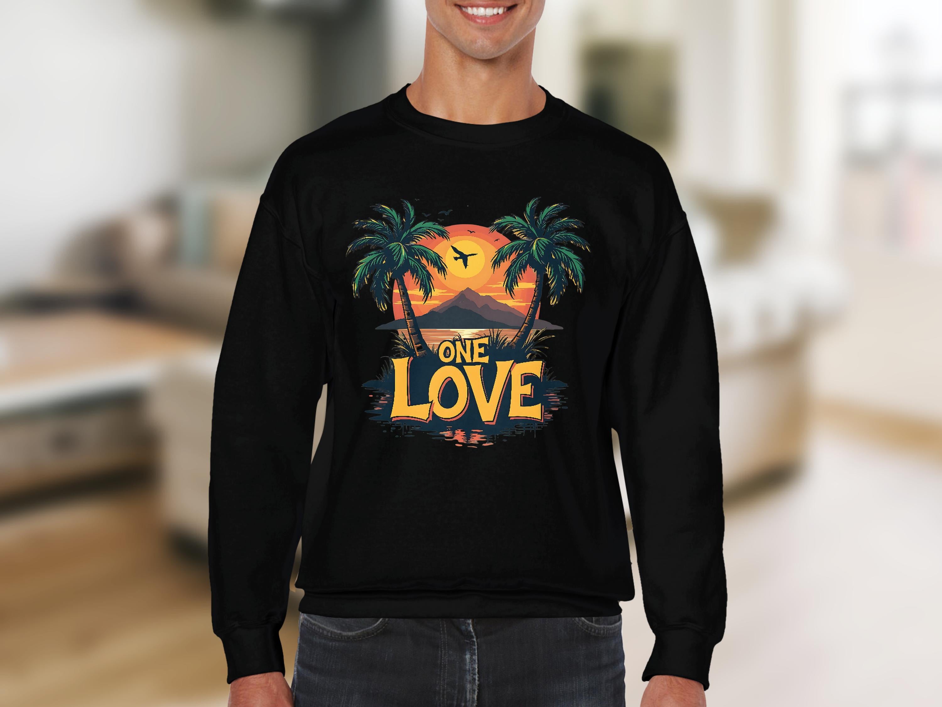 A person wears a black sweatshirt from Garment Graphics One Love Sweatshirts collection. It features a tropical sunset design with palm trees, an airplane silhouette, and ONE LOVE text. Set indoors with a blurred background, the sweatshirt offers unisex sizing for everyone.