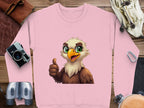 A pink Garment Graphics sweatshirt, featuring a cheerful cartoon eagle giving a thumbs-up, is centered on a wooden surface. It’s surrounded by a vintage camera, binoculars, leather pouch, canvas bag, and carabiner clip. This unisex piece pairs playful style with versatile accessorizing.