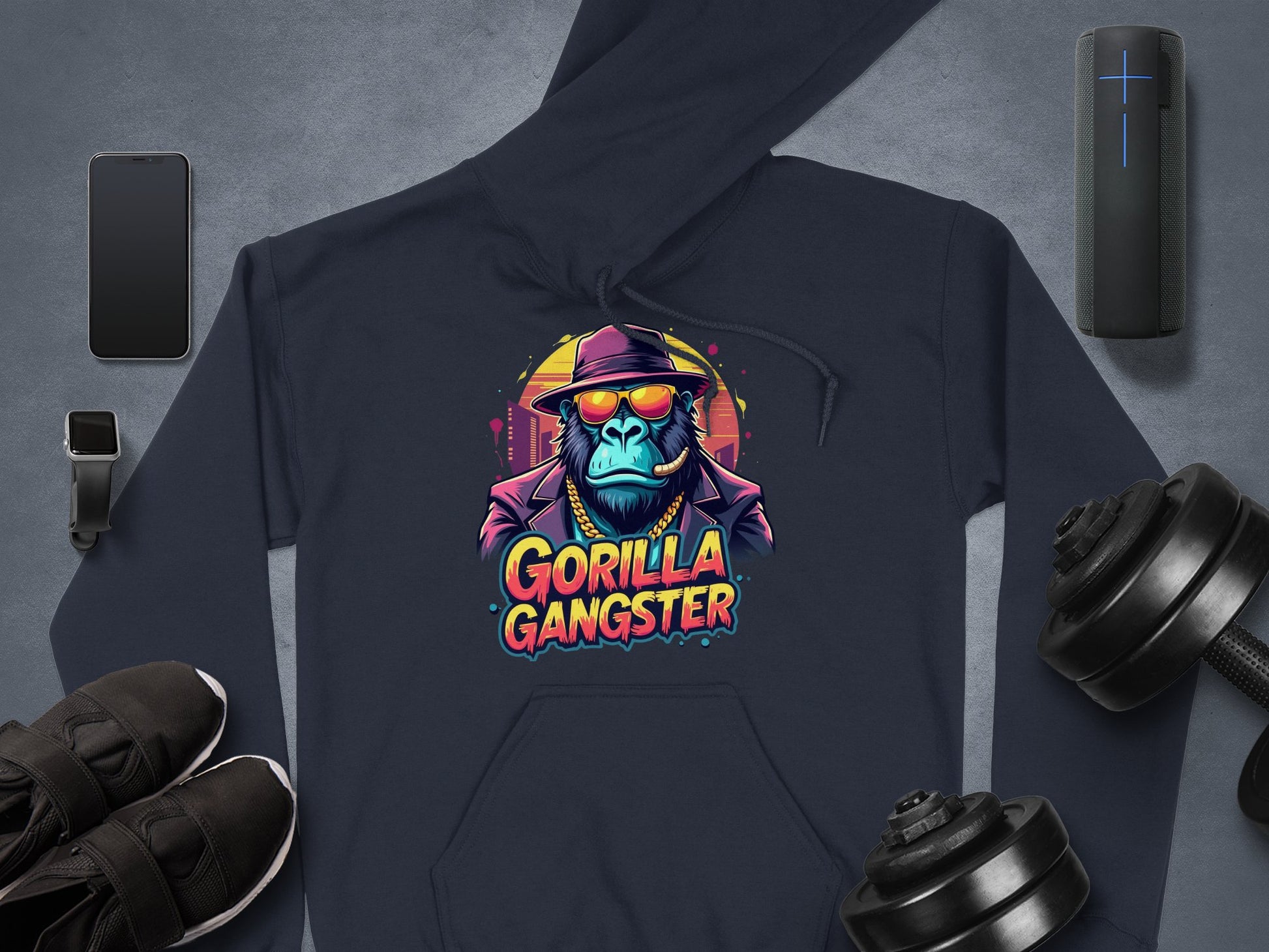 Garment Graphics presents a blue hoodie with a vibrant cartoon gorilla in a suit, hat, and sunglasses labeled Gorilla Gangster. Encircled by shoes, smartwatch, smartphone, speaker, and dumbbells—perfect for striking Gorillas artwork fans.