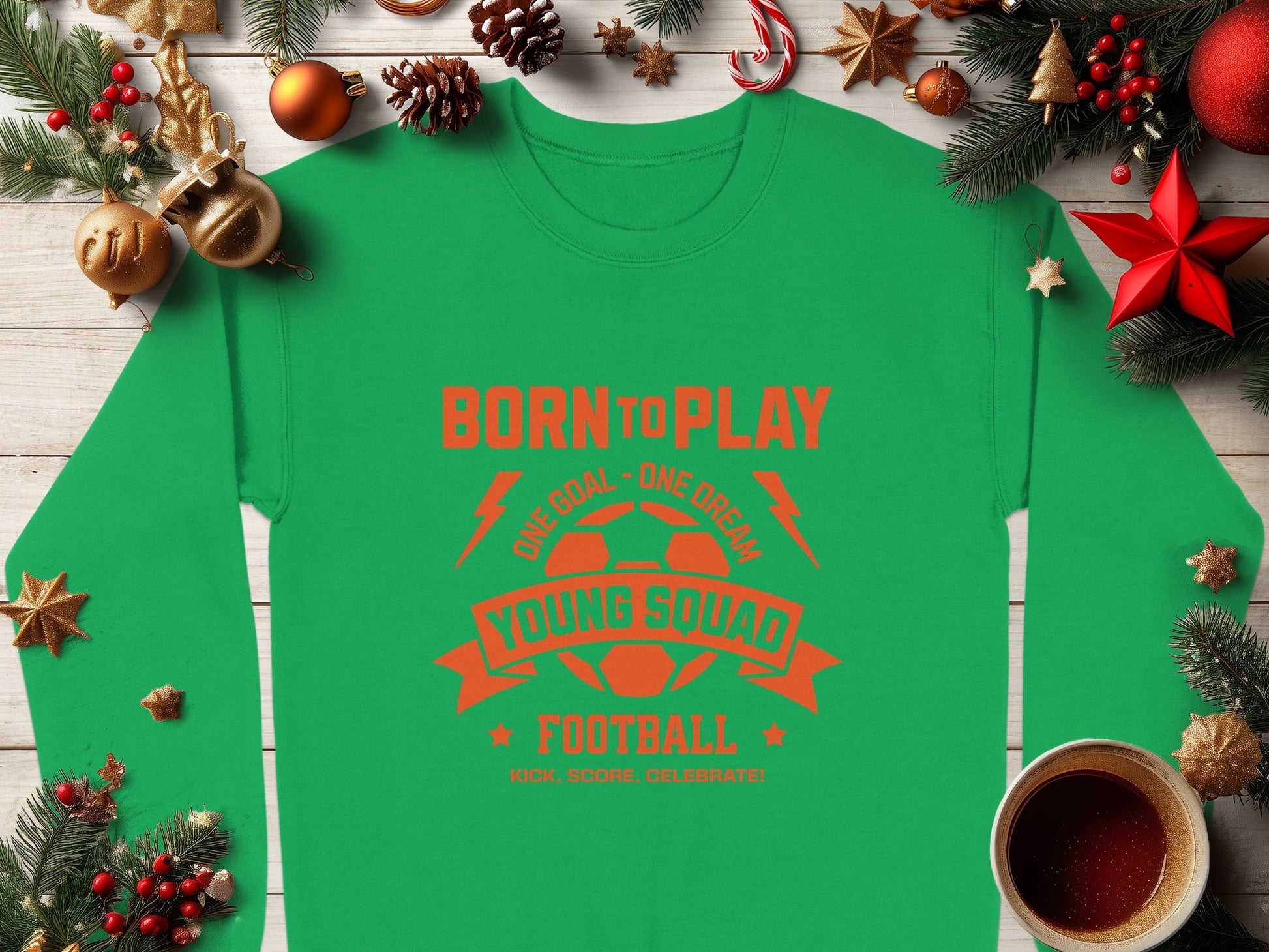 The Garment Graphics green football sweatshirt features orange text and a soccer ball graphic saying Born to Play, One Goal - One Dream, Young Squad Football, Kick, Score, Celebrate. Ideal for young aspiring footballers with festive background elements. Available in unisex sizing.