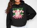 Someone wearing a black hoodie from Garment Graphics Wild Side Hoodies collection, featuring Hands off! beneath a stylized figure in a hat and bandana, decorated with flowers and hearts. Wild Girl is playfully positioned above off! in vibrant pink and green.