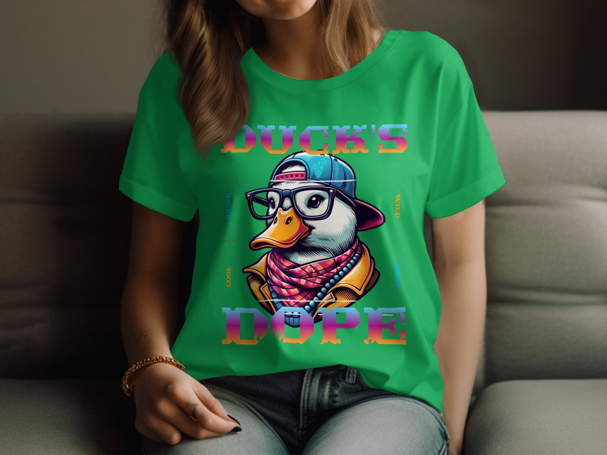 A person relaxes on a gray sofa in a green T-shirt from Garment Graphics, showcasing a duck with cap, glasses, and scarf labeled Ducks Dope in vibrant letters. Their long hair falls over their shoulders, completing the look.