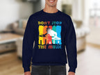 A person wears a Garment Graphics navy blue sweatshirt featuring a vibrant DJ design and the phrase Dont Stop the Music, set against a backdrop of bright paint strokes and abstract designs. A must-have for music enthusiasts.