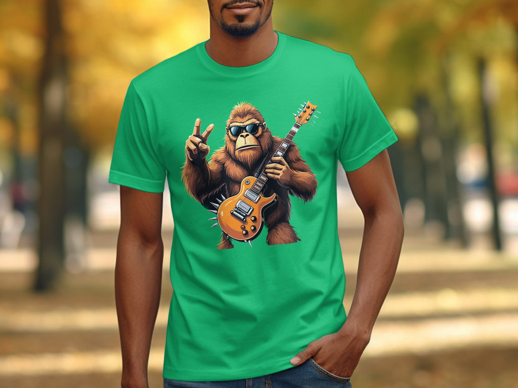 A person in a Garment Graphics green T-shirt with a cartoon Bigfoot playing an electric guitar and making a peace sign stands on an autumn-leaf-lined path, an ideal scene for music lovers.