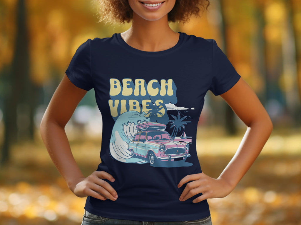 A person wears a navy Garment Graphics T-shirt featuring Beach Vibes with a retro design of a vintage car, palm trees, and wave. The setting is a blurred park adorned with autumn foliage, perfectly capturing surf-inspired nostalgia.