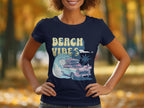 A person wears a navy Garment Graphics T-shirt featuring Beach Vibes with a retro design of a vintage car, palm trees, and wave. The setting is a blurred park adorned with autumn foliage, perfectly capturing surf-inspired nostalgia.