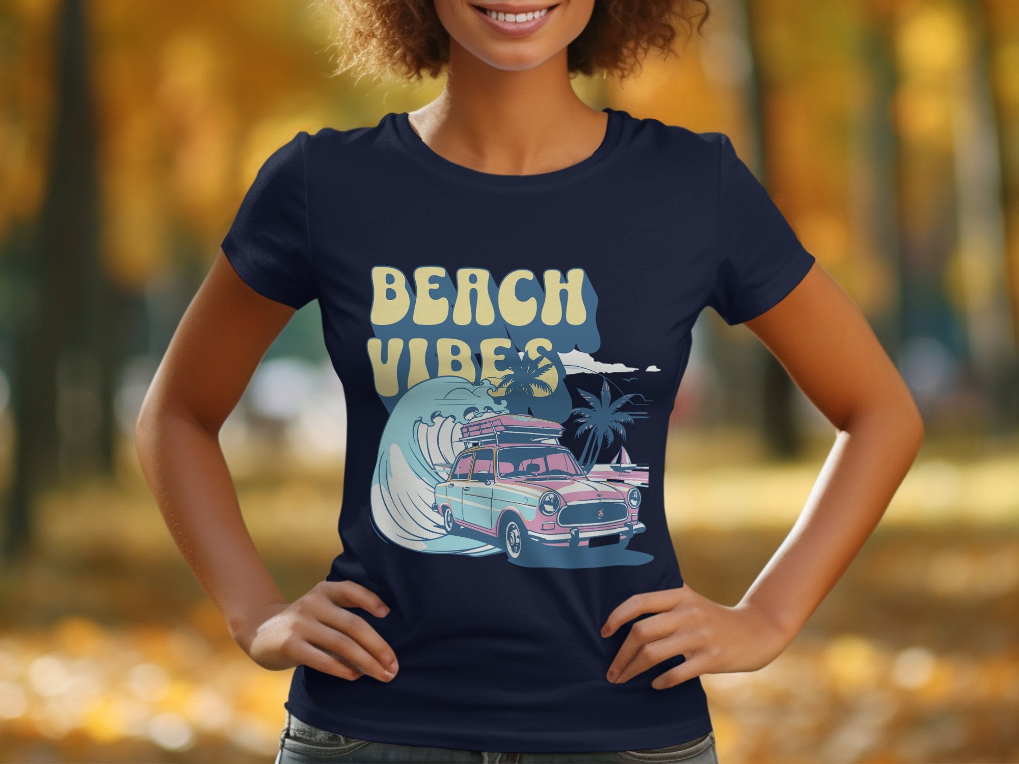A person wears a navy Garment Graphics T-shirt featuring Beach Vibes with a retro design of a vintage car, palm trees, and wave. The setting is a blurred park adorned with autumn foliage, perfectly capturing surf-inspired nostalgia.