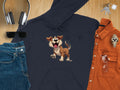 A Garment Graphics navy blue cartoon dog hoodie, ideal for dog lovers, is displayed on wood. Its surrounded by jeans, headphones, sunglasses, keys, a watch, an orange button-up shirt, and aviator glasses—a perfect arrangement for fans of fun design hoodies.