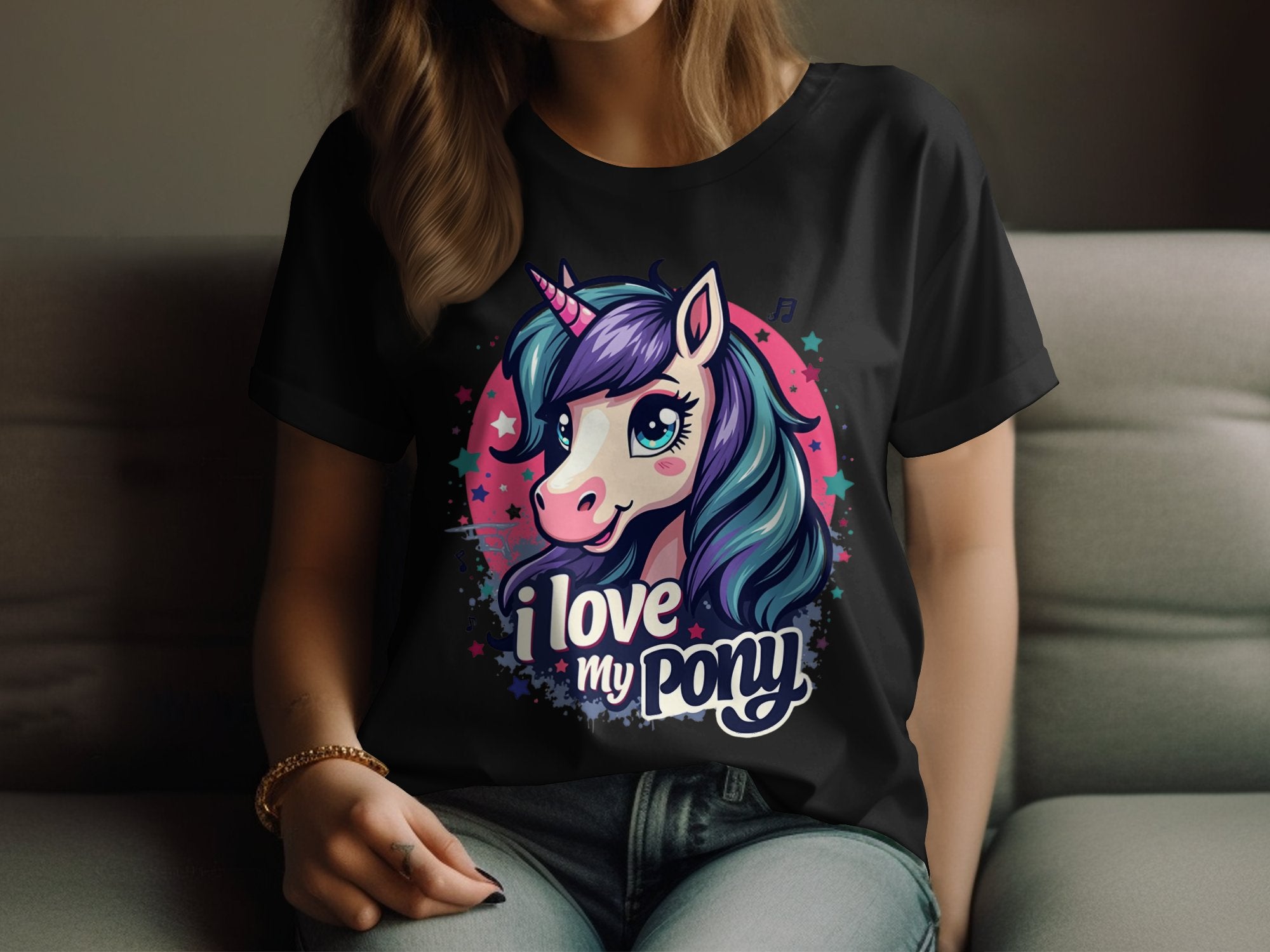 A person relaxes on a couch wearing a Garment Graphics black t-shirt adorned with a vibrant unicorn graphic: blue and purple mane, pink horn, I Love My Pony text. Ideal for unicorn fans, it features stars and a pink circle as they rest their hand on their knee.