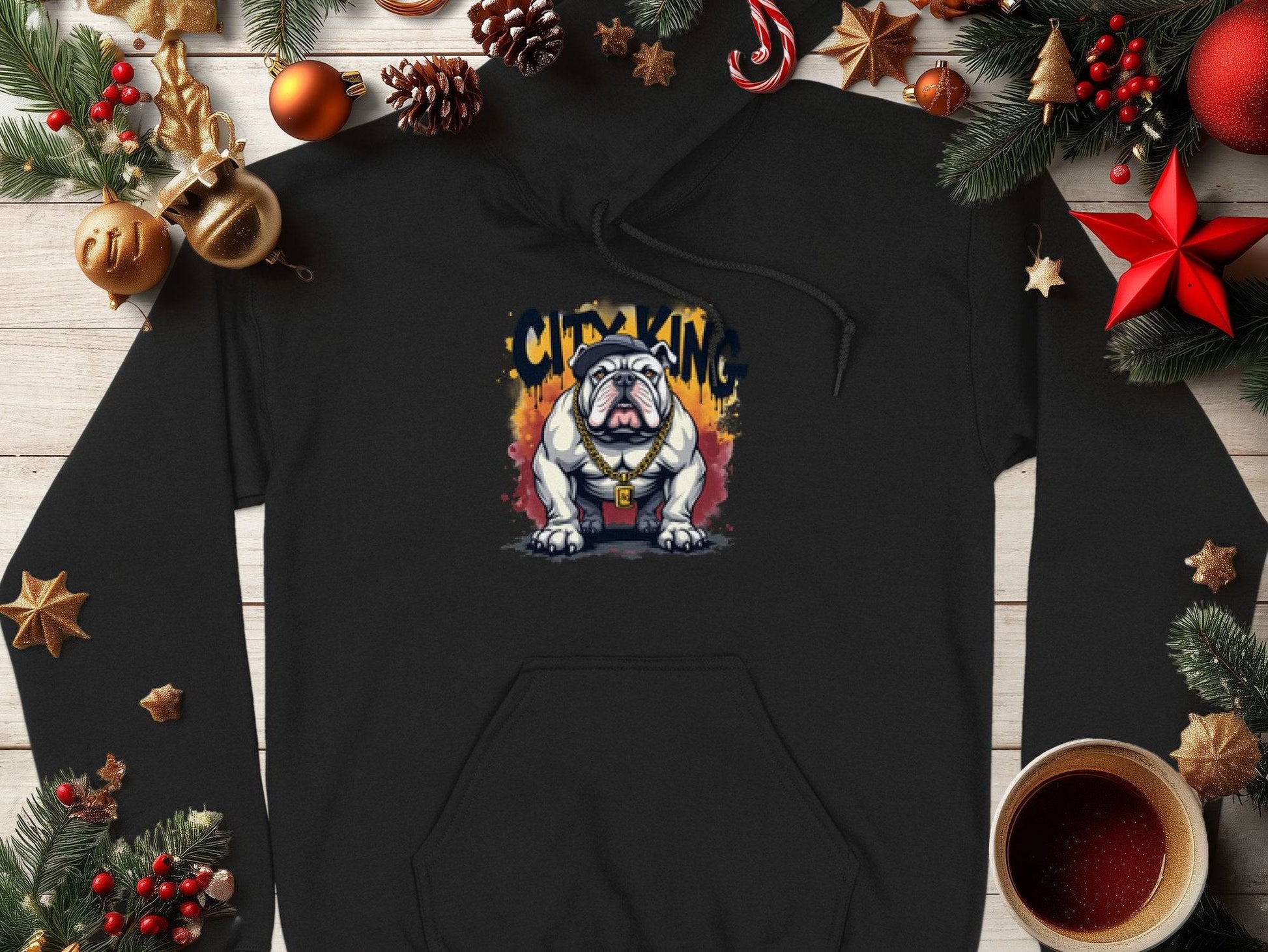 The Garment Graphics black hoodie showcases a graphic bulldog with sunglasses and a crown, surrounded by City King in graffiti style. Ideal for casual wear, it features a classic fit and is displayed on a wooden table adorned with Christmas decorations and a cup of hot beverage.