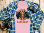 A Garment Graphics pink T-shirt with bold bull illustrations and BULLOCKS is laid over a plaid shirt. Nearby, a camera, black headphones, and a white bottle are artfully arranged on a wooden surface.