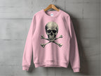 A bold pink sweatshirt by Garment Graphics, featuring an edgy skull and crossbones graphic, hangs on a wooden hanger against a concrete wall.
