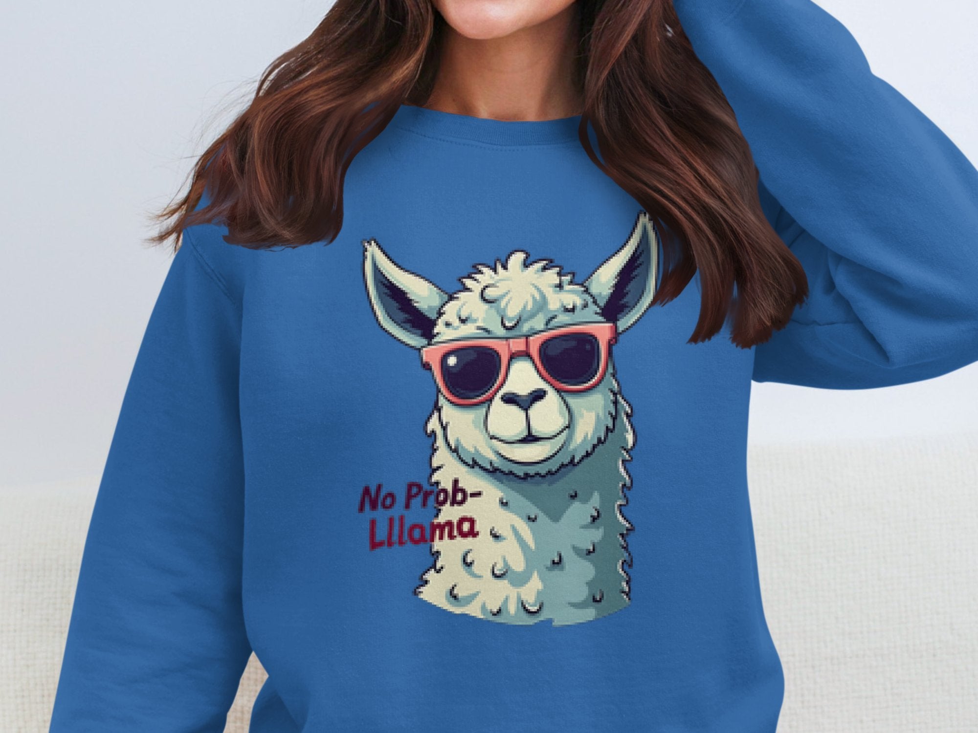 Wearing Garment Graphics No Prob-Llama sweatshirt featuring a cartoon llama in sunglasses, a woman poses with her arm near her head, highlighting the unisex fit and playful style as her hair falls over her shoulders.