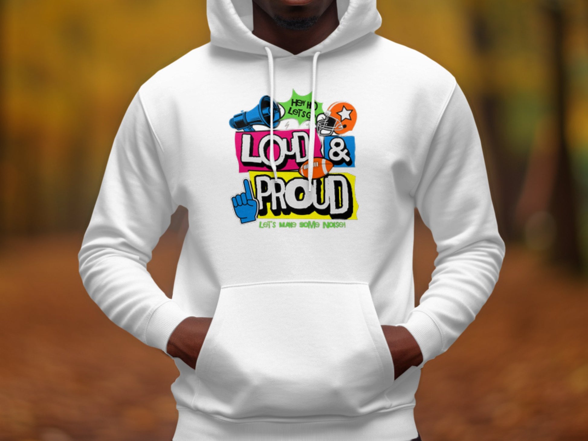 A person wears a Garment Graphics white hoodie featuring vibrant cartoon-style text and graphics, including Loud & Proud, with icons like a shoe, star, and raised fist. The scene is set outdoors against blurred fall foliage.