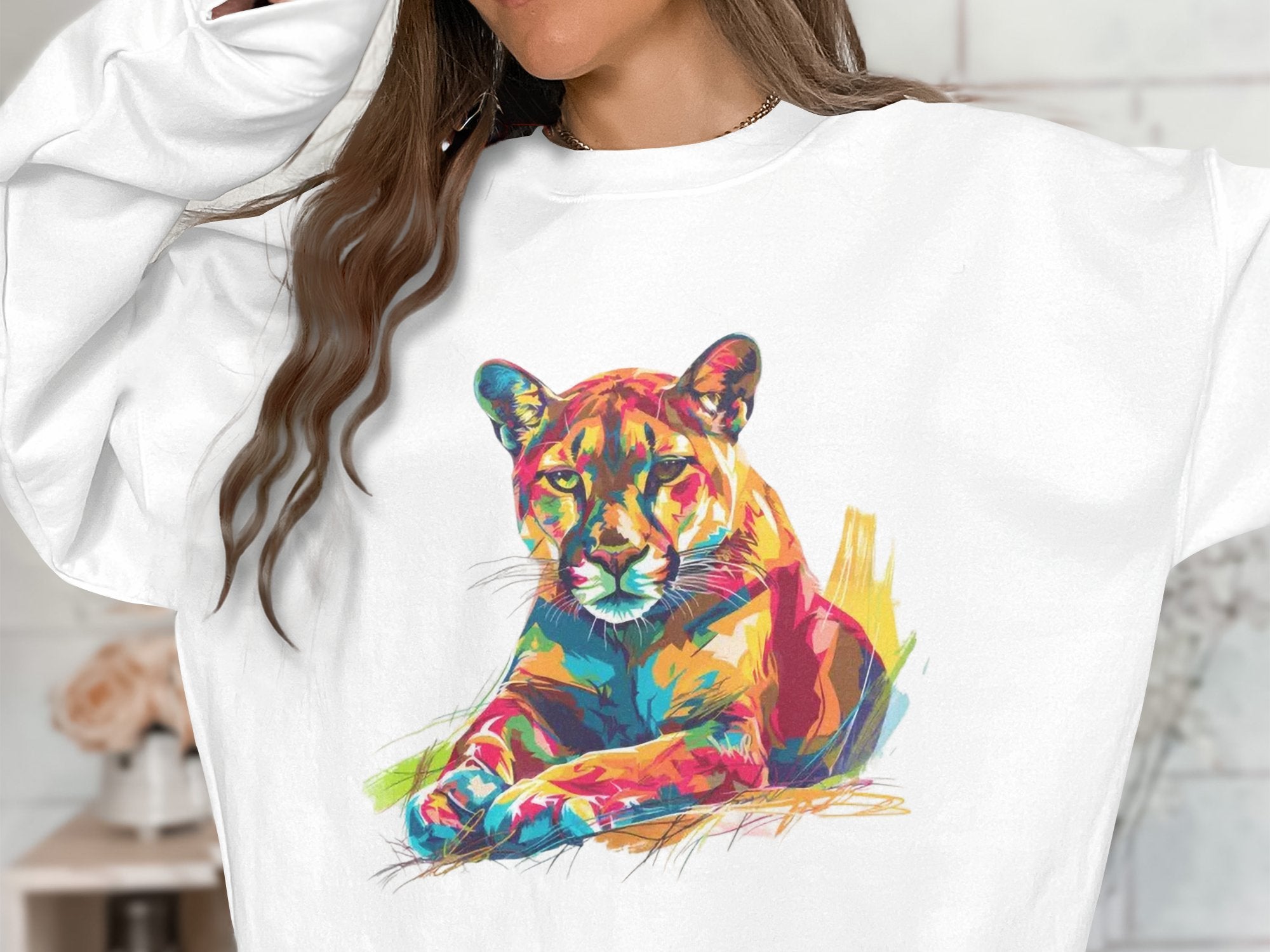 A person wears a unisex white sweatshirt by Garment Graphics, featuring a vibrant reclining lion in orange, blue, green, and red. The unique big cat design captures attention effortlessly, with the persons face unseen.