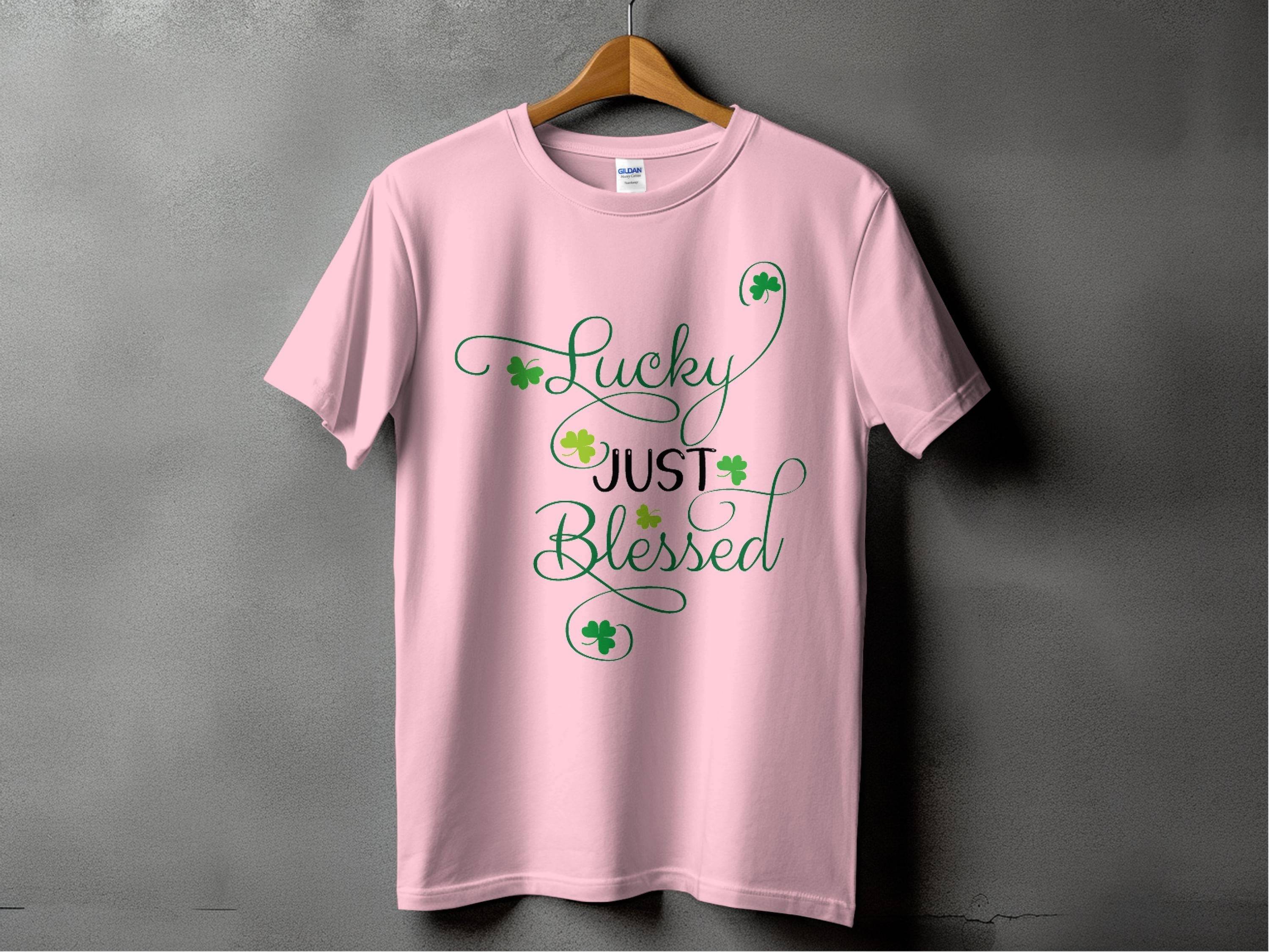 The Royal Mail - 24 Tracked t-shirt is a classic fit in pink with the phrase Lucky Just Blessed, featuring green shamrock motifs and decorative swirls, set against a dark gray background to blend style and luck.