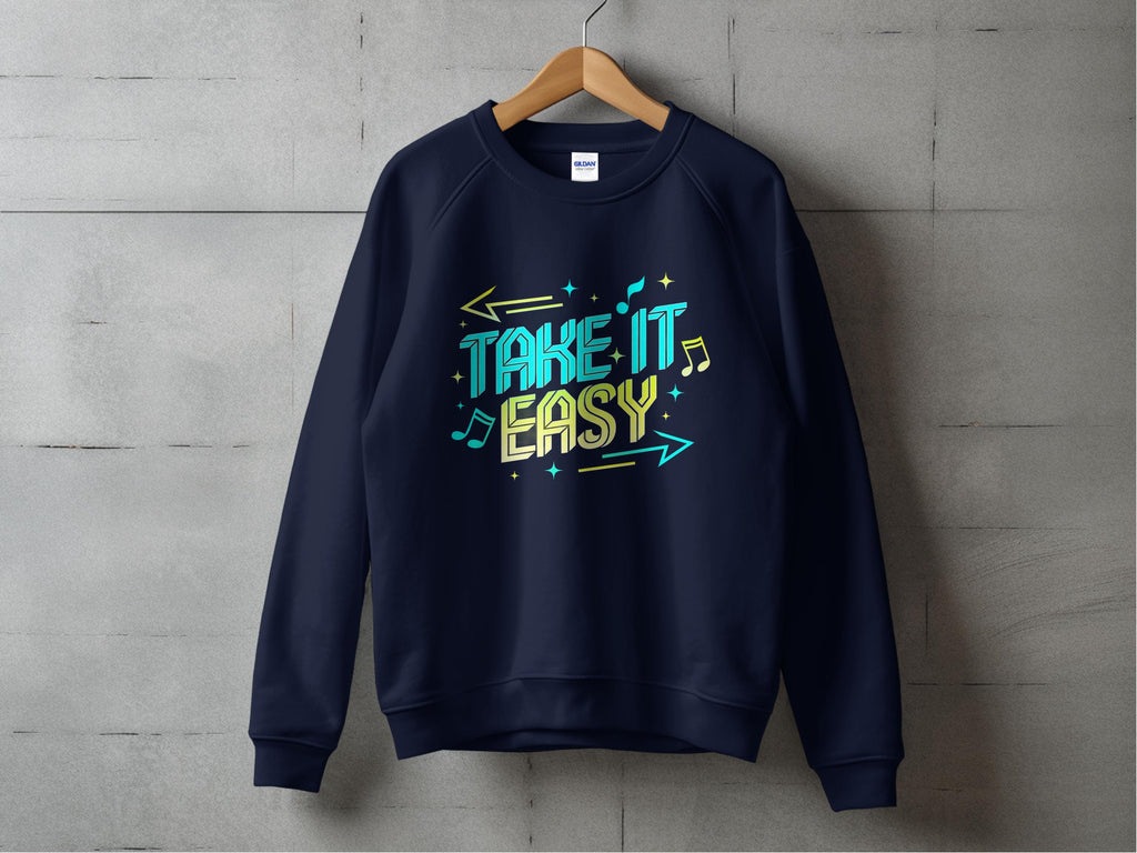 A black sweatshirt hangs on a wooden hanger against a gray concrete wall. Designed by Garment Graphics, it features Take It Easy in colorful letters with musical notes and arrows. Unisex sizing makes it ideal for sharing your laid-back style.