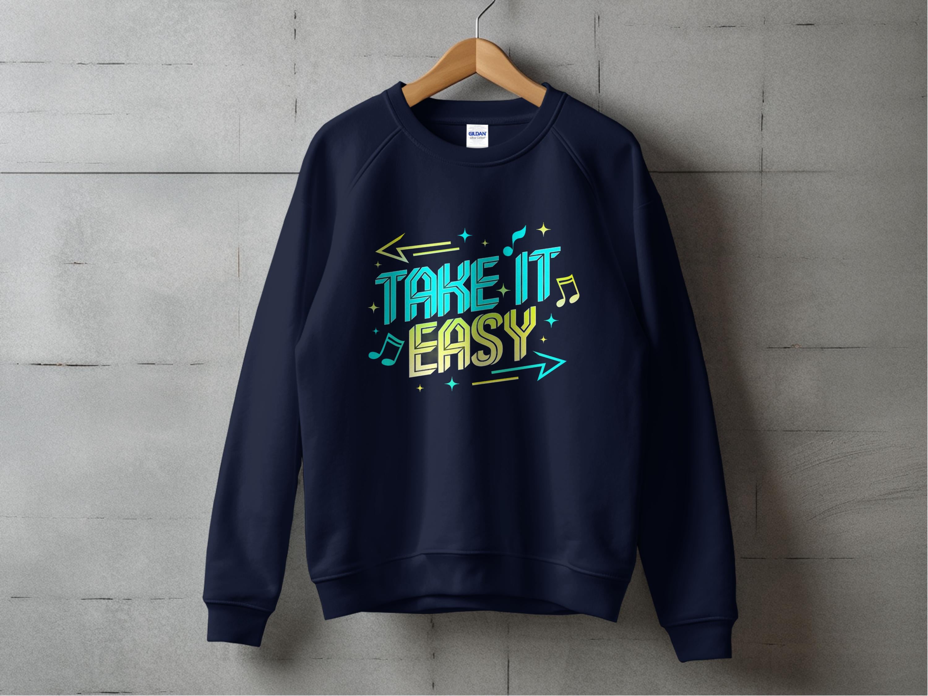 A black sweatshirt hangs on a wooden hanger against a gray concrete wall. Designed by Garment Graphics, it features Take It Easy in colorful letters with musical notes and arrows. Unisex sizing makes it ideal for sharing your laid-back style.