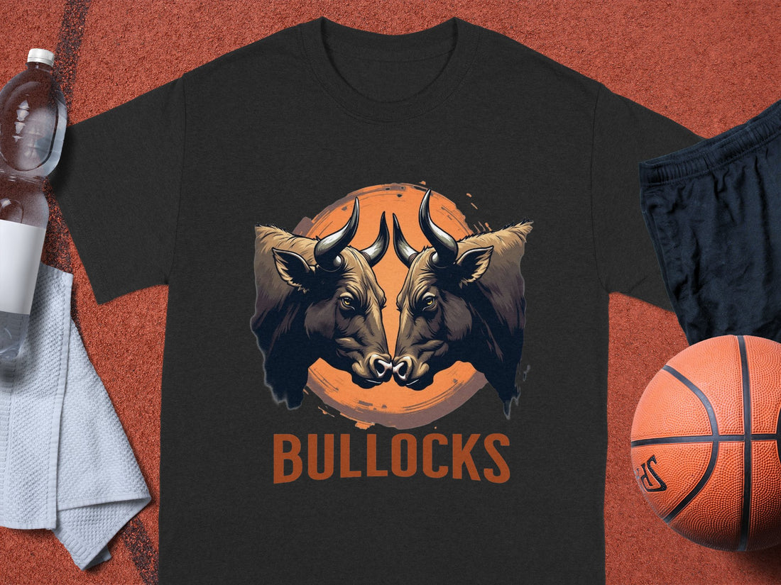 A Garment Graphics black t-shirt from the Bullocks Pintable collection features two bulls facing off in front of an orange circle with BULLOCKS below. Perfect for family sizing, the classic fit is pictured on a sports court beside a basketball, shorts, water bottle, and towel.