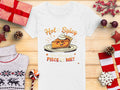 A womens white T-shirt from Garment Graphics, with a cartoon pumpkin pie graphic and the text Hot & Spicy, You Wanna a Piece of Me? is displayed on a wooden surface. Ideal for casual outings, its surrounded by holiday-themed items: sweater, gifts, pinecones, candy, and ornaments.