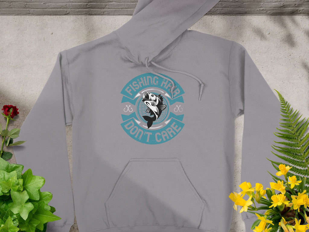 Garment Graphics graphic hoodie displays Fishing Hair Dont Care in aqua and white with a fish design. Set on concrete, its surrounded by green, yellow plants, and vibrant red flowers, making it ideal for any passionate angler.