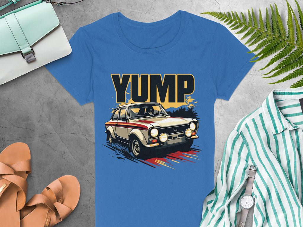 A bold graphic vintage car with YUMP is featured on this blue t-shirt by Garment Graphics. It is displayed on a gray background, accompanied by a striped shirt, brown sandals, light blue handbag, watch, and green fern leaves.