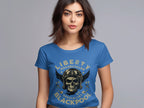 A woman with long dark hair wears a blue Garment Graphics t-shirt featuring Blackpool-themed design elements like a skull and wings motif. The text Liberty Motorcycles Specialist Blackpool is displayed as she stands against a plain gray background.