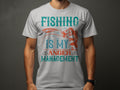 A fishing enthusiast wears a Garment Graphics gray T-shirt featuring a fish with the slogan Fishing is my Anger Management in vibrant teal and orange.