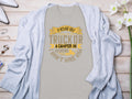 Light gray Garment Graphics t-shirt with the text If hes got golf clubs in his truck or a camper in his driveway, dont hire him in yellow and gray. Ideal for camping or golf fans, styled with a cardigan and surrounded by white flowers and jewelry.