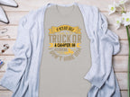 Light gray Garment Graphics t-shirt with the text If hes got golf clubs in his truck or a camper in his driveway, dont hire him in yellow and gray. Ideal for camping or golf fans, styled with a cardigan and surrounded by white flowers and jewelry.