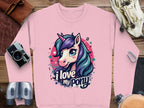 The Garment Graphics pink sweatshirt showcases a cartoon unicorn with a colorful mane and horn, surrounded by stars and music notes, with I love my pony text. Ideal for graphic sweatshirt fans, its styled flat beside a camera, binoculars, and other accessories.