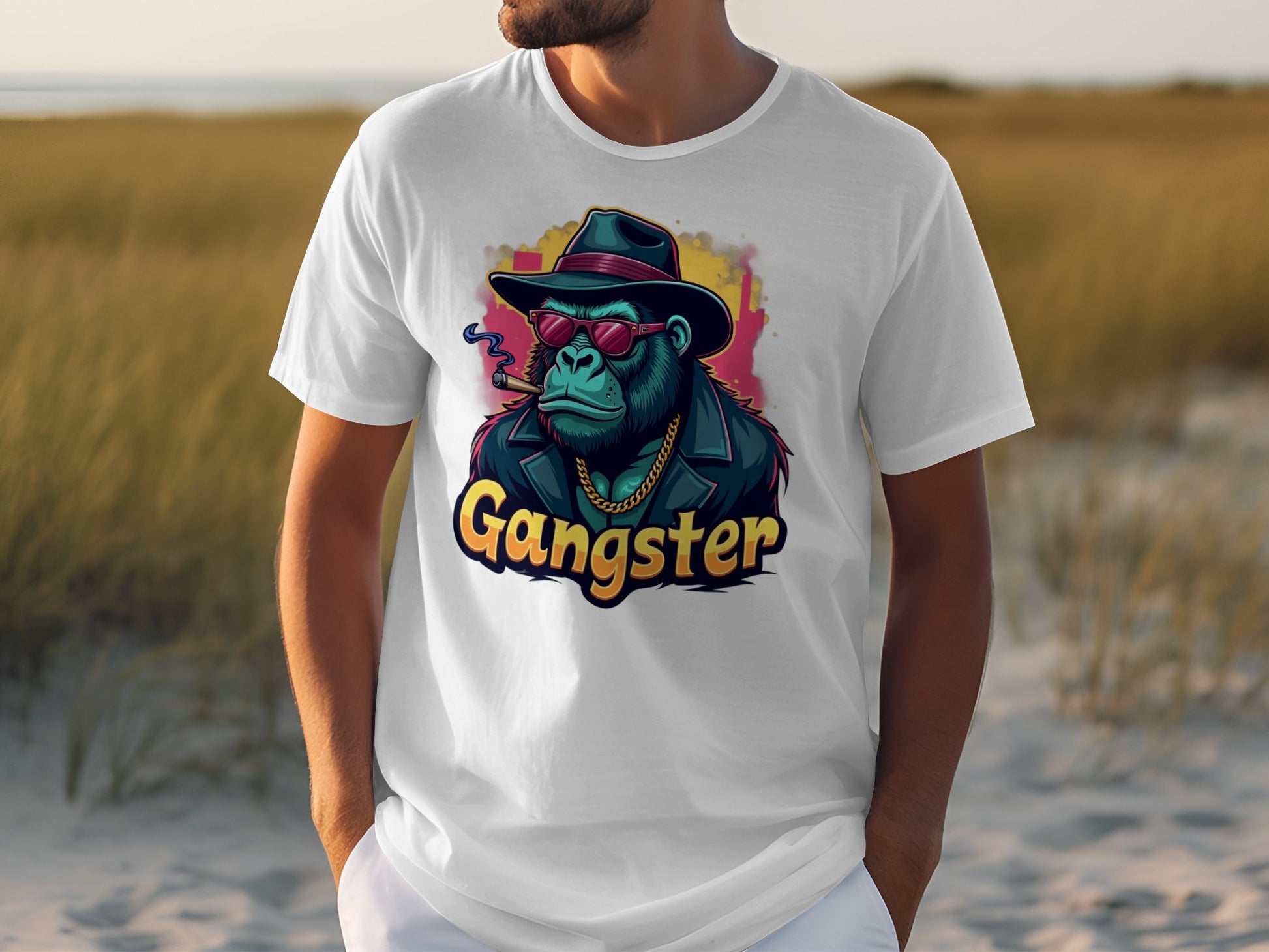 Someone wearing a classic fit Gangster Gorilla T-Shirt by Garment Graphics. The white tee showcases an urban illustration of a gorilla as a gangster with a hat, sunglasses, and gold chain. Gangster is prominently displayed beneath amidst grass and sand.