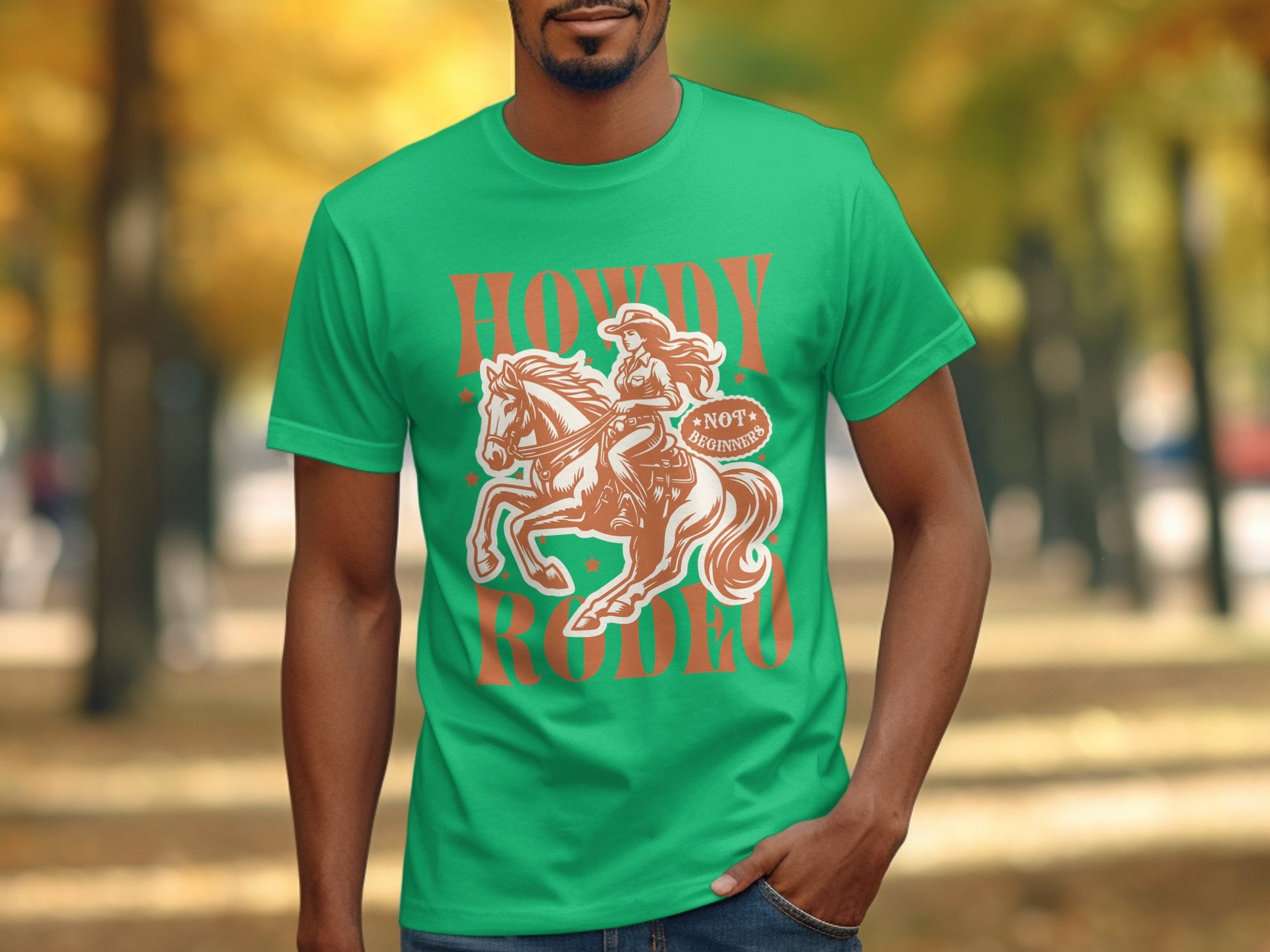 A person wearing a green Garment Graphics T-Shirt features a cowboy riding a horse with the words Howdy Rodeo in bold. The background artistically blurs trees with autumn leaves, crafting an ideal scene for rodeo enthusiasts.