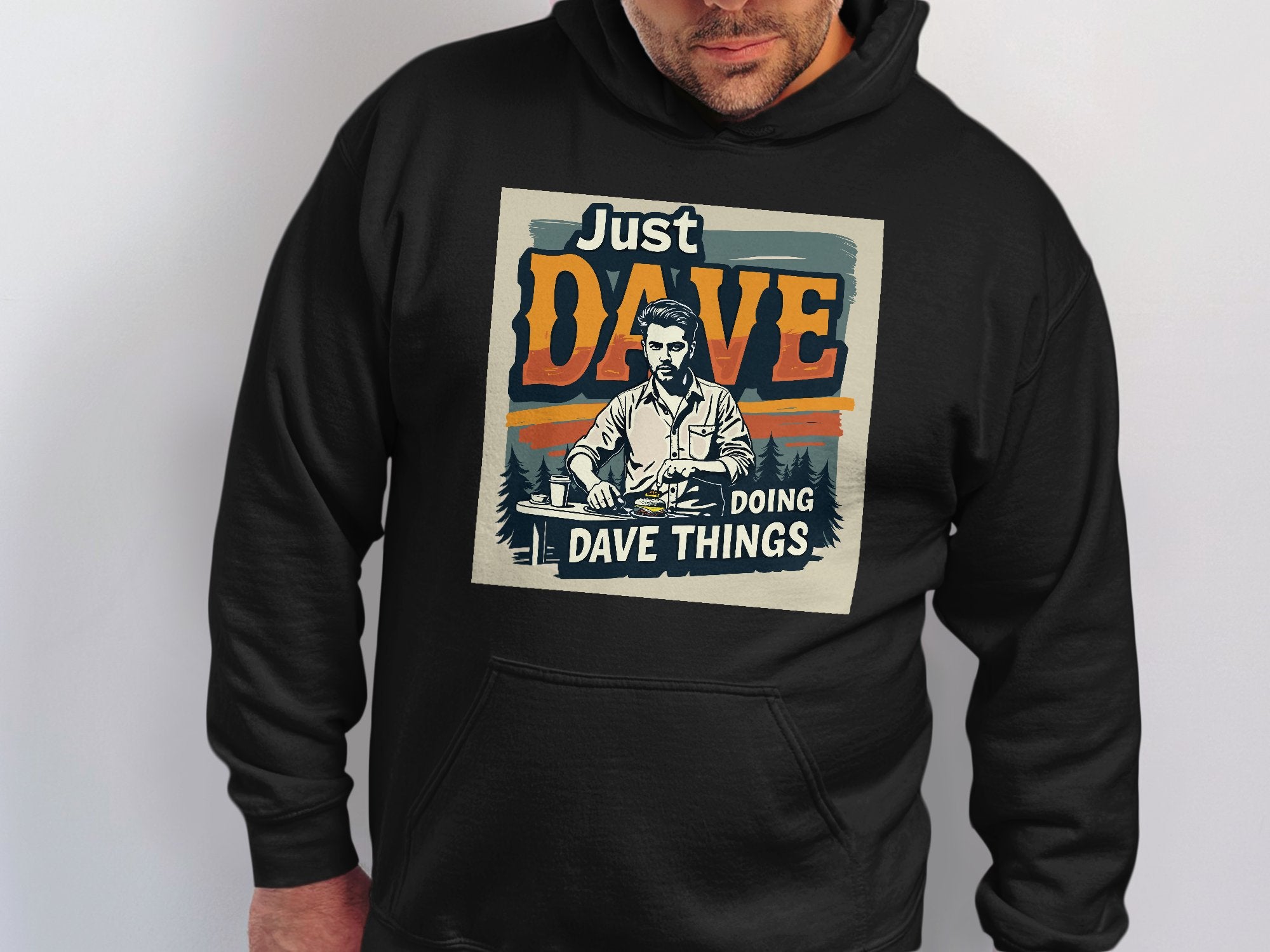 A person is seen in a Garment Graphics black graphic hoodie made from medium-heavy fabric, showcasing an illustration of a man alongside the text Just Dave Doing Dave Things on a plain background.